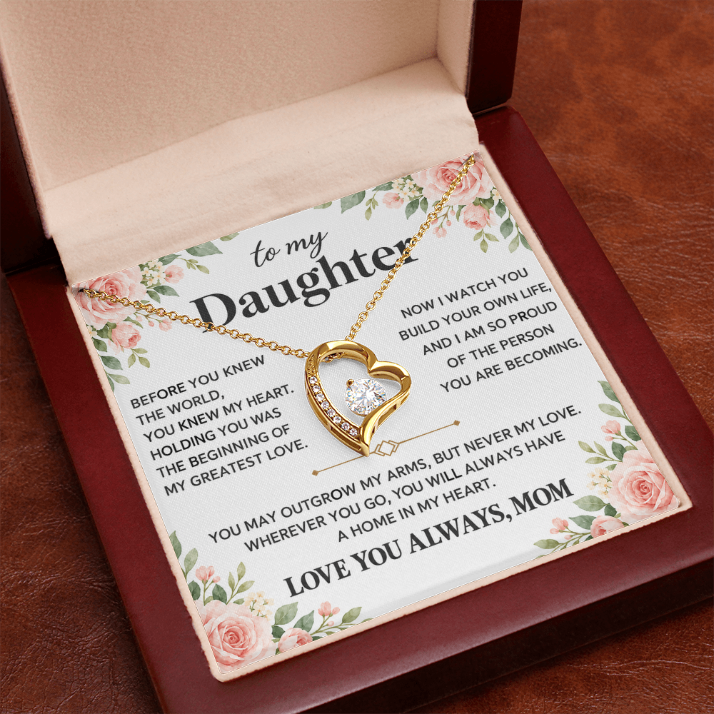 Gold-tone heart pendant necklace in an open red box held in a hand against a blue background.