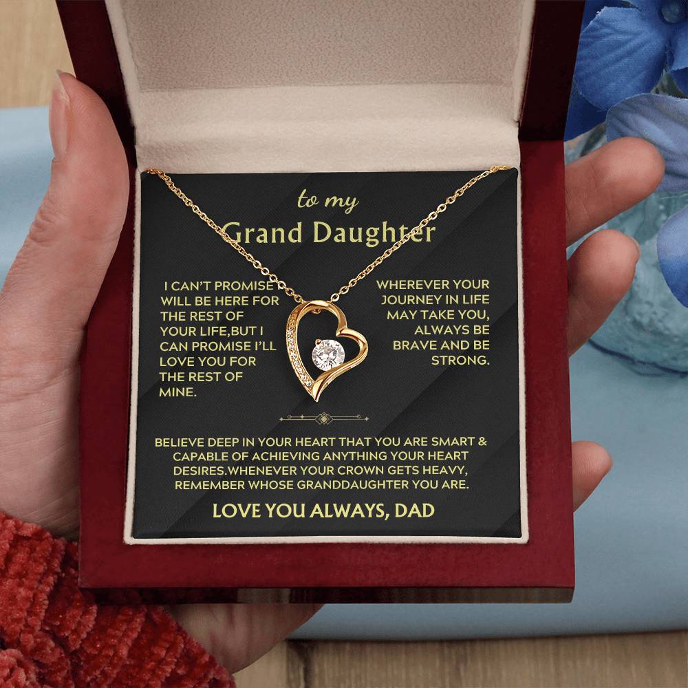 Gold-tone heart necklace on a black Grand Daughter message card in an open burgundy box held in one hand.