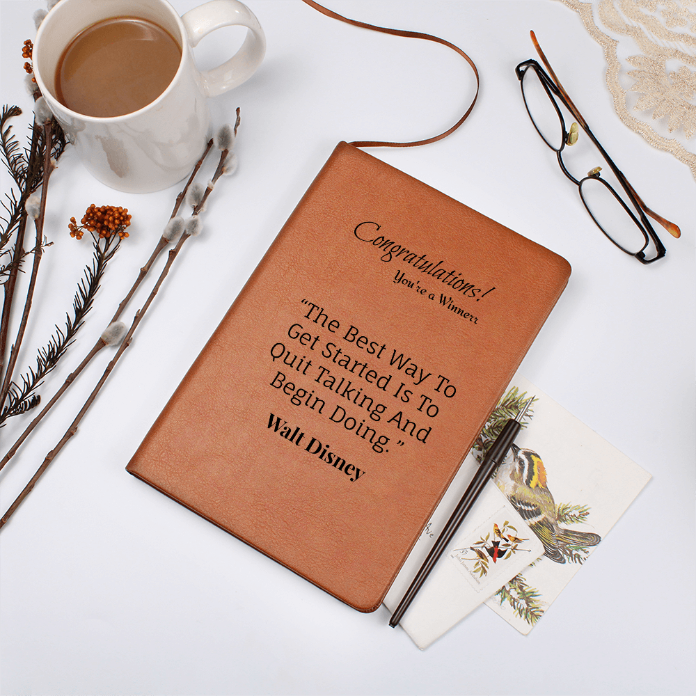 Tan journal with winner message beside a coffee cup, glasses, pen and illustrated cards