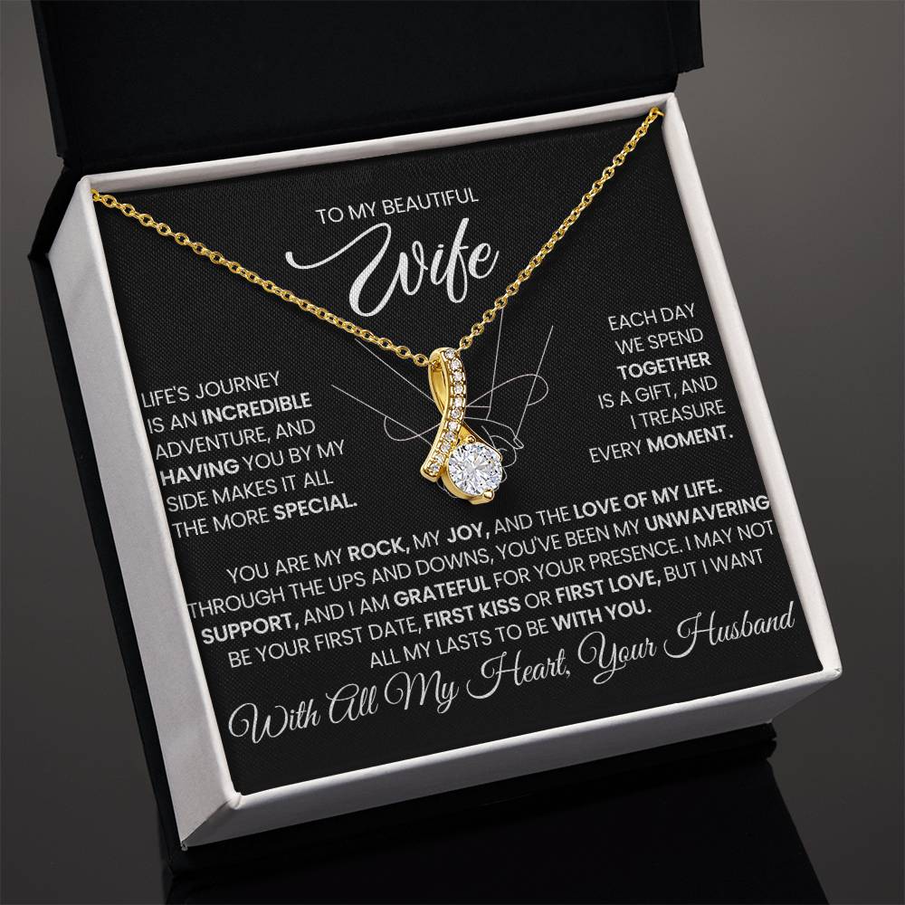 Angled gold-tone ribbon pendant necklace presented in an open white jewellery box.