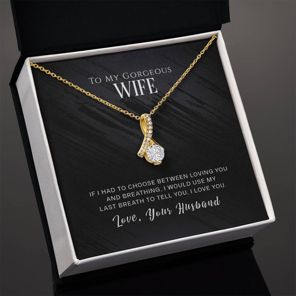 Gold-tone ribbon pendant necklace shown at an angle in an open white presentation box