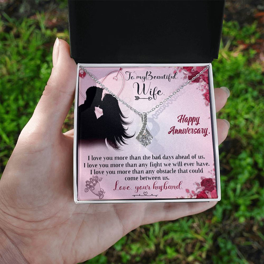 Silver-tone ribbon pendant necklace in its message card box, held outdoors in one hand.
