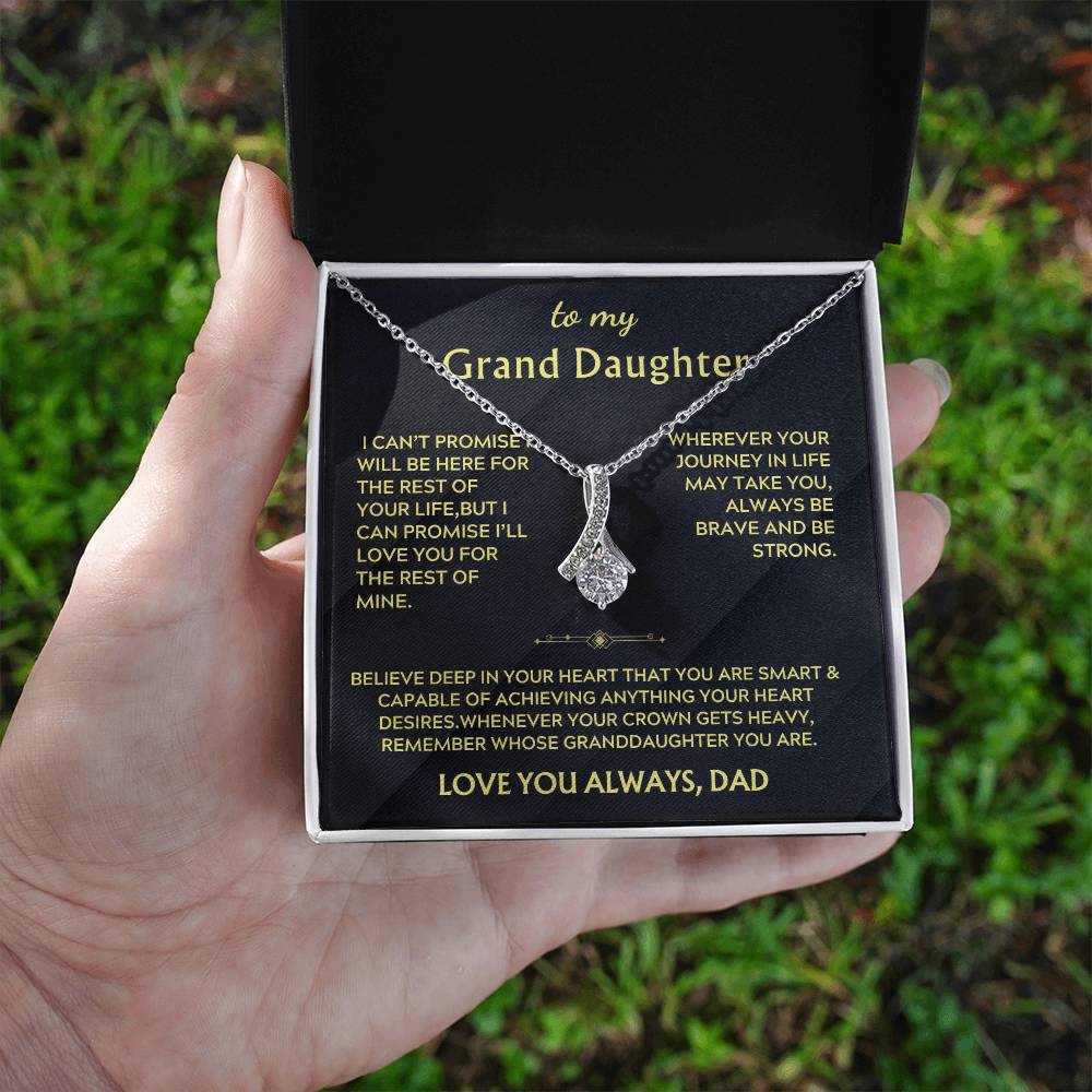 Open jewellery box held outdoors, showing a silver ribbon pendant and granddaughter message card.
