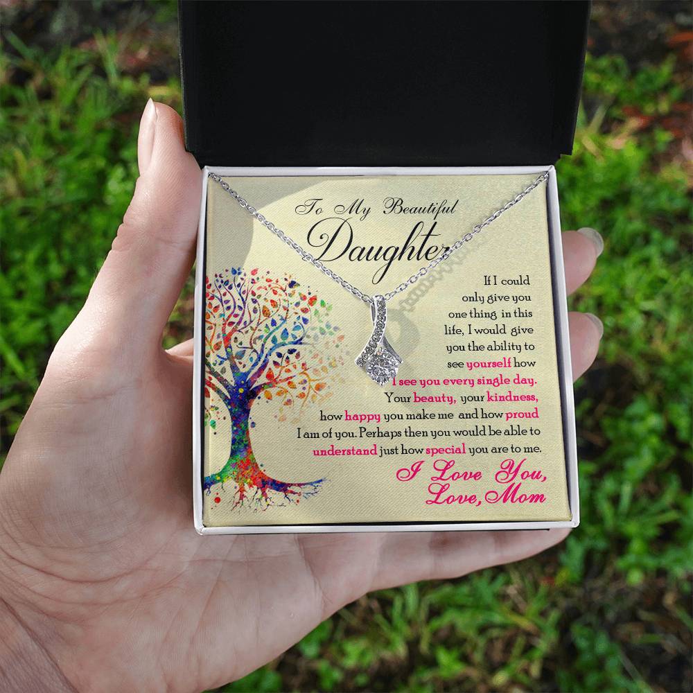 A hand holds an open white jewellery box showing the silver-tone necklace and daughter message card.