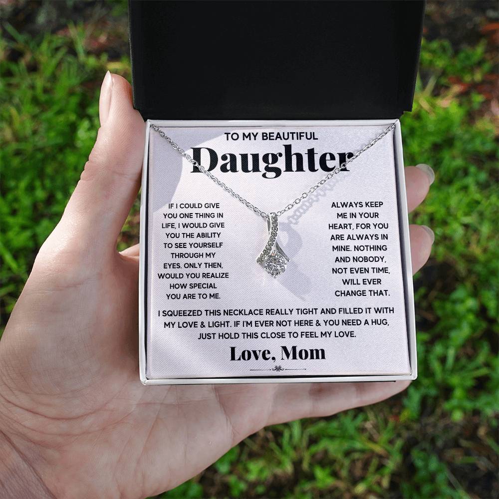 Hand holding an open necklace box showing a daughter message card outdoors
