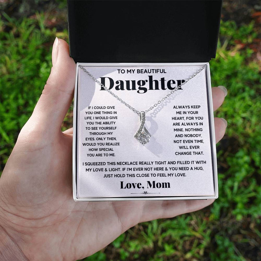 Hand holding an open necklace box showing a daughter message card outdoors