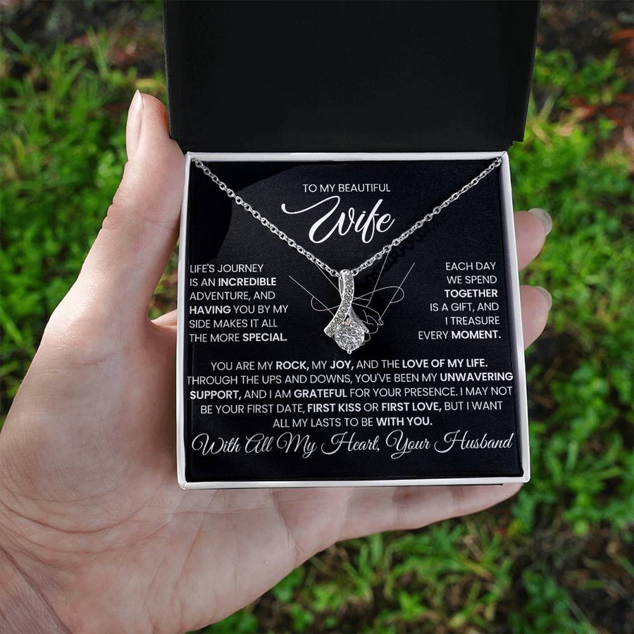 Silver-tone ribbon pendant necklace and message card held in an open white box outdoors.