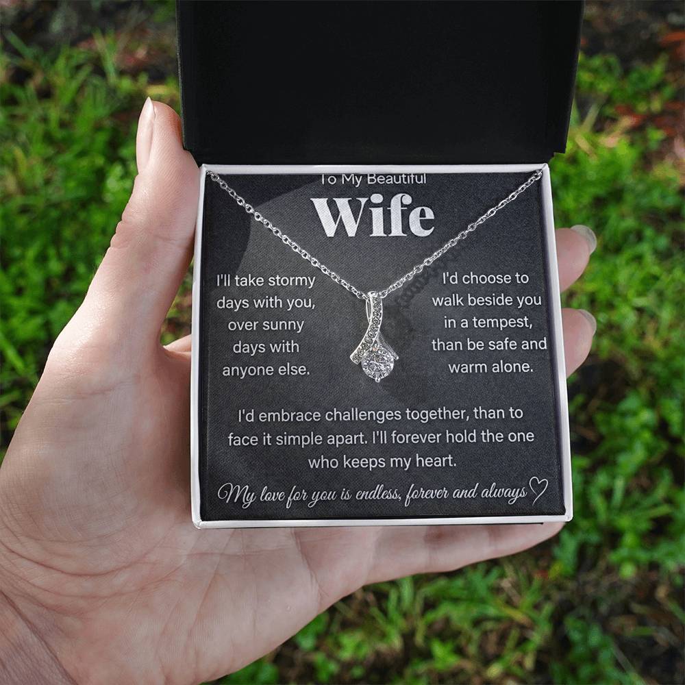 Hand holding an open white box with a silver-tone necklace and wife message card outdoors
