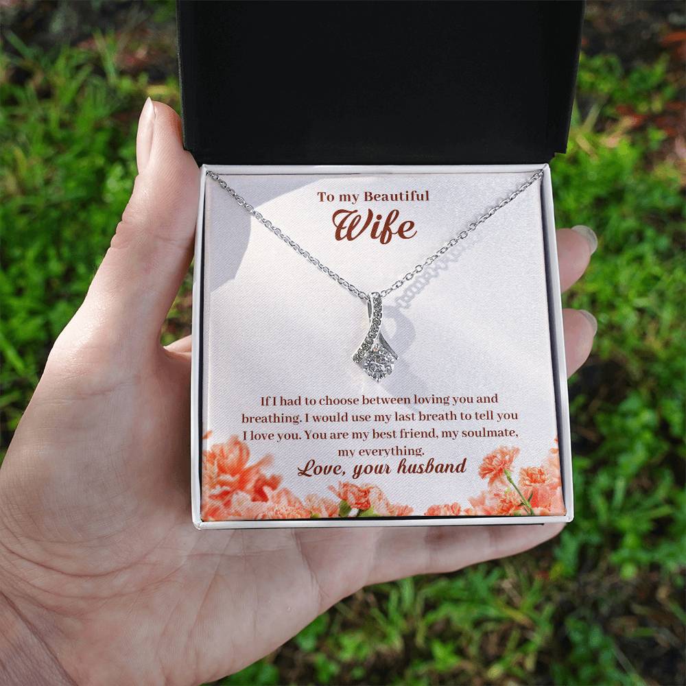 A hand holds an open jewellery box showing the wife message card and silver-tone pendant outdoors.