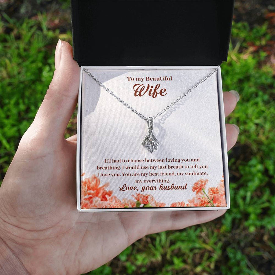 A hand holds an open jewellery box showing the wife message card and silver-tone pendant outdoors.