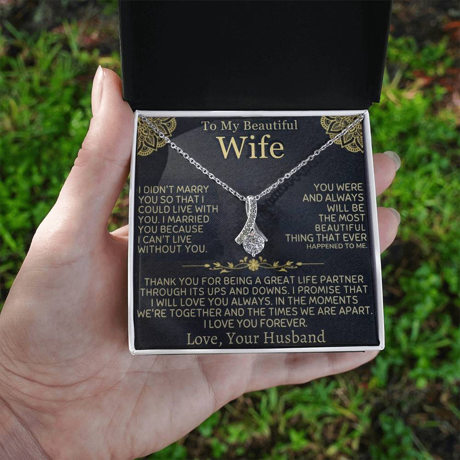 A hand holds an open gift box containing the wife message card and silver-tone necklace outdoors.