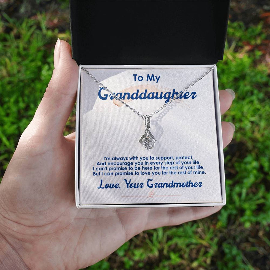 A hand holds an open jewellery box showing a silver-tone pendant necklace and message card.