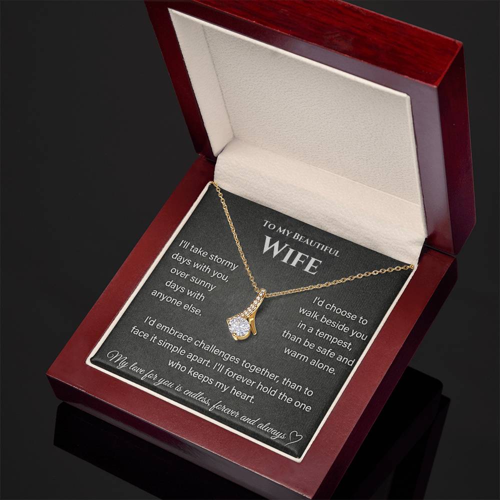 Angled view of a gold-toned necklace resting on the wife message card inside a mahogany-style box.