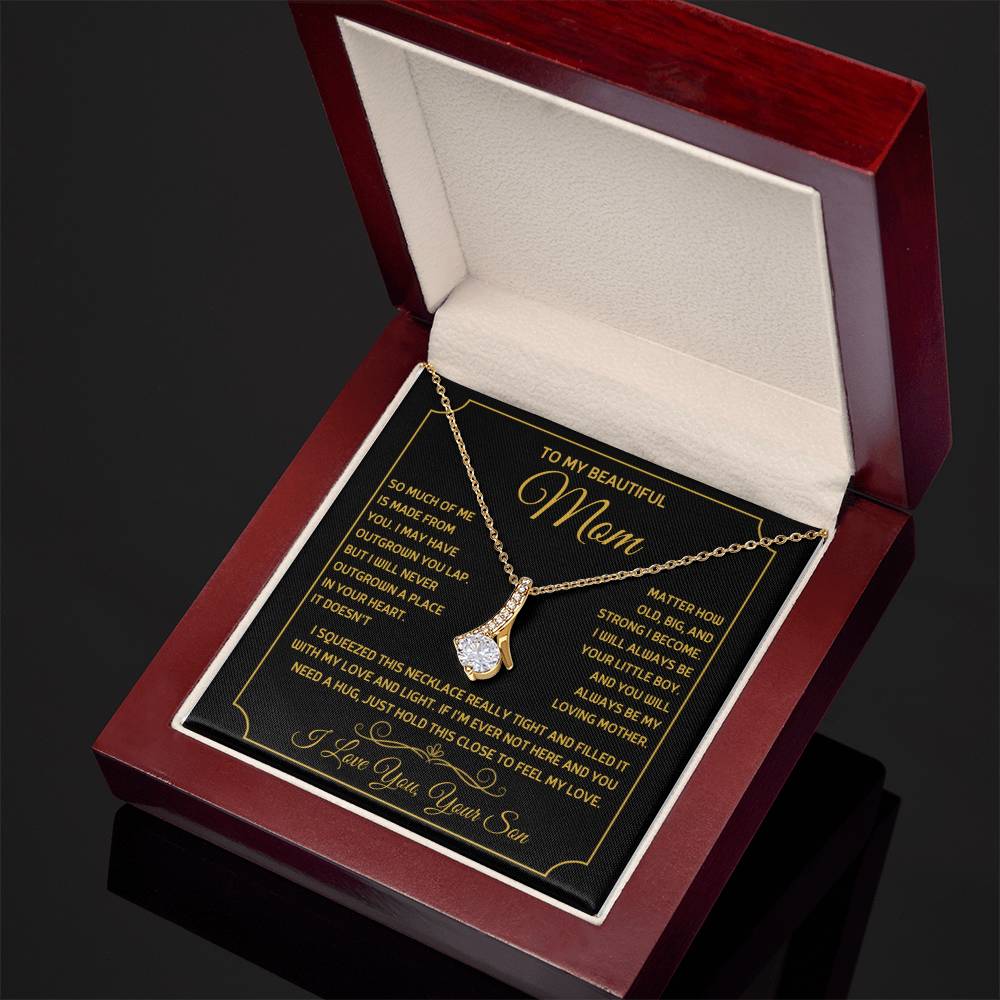 Angled view of a gold ribbon pendant necklace and message card in a mahogany box