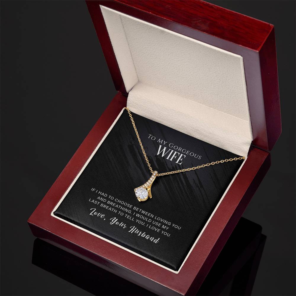 Gold-tone ribbon pendant necklace shown at an angle inside an open mahogany-style box