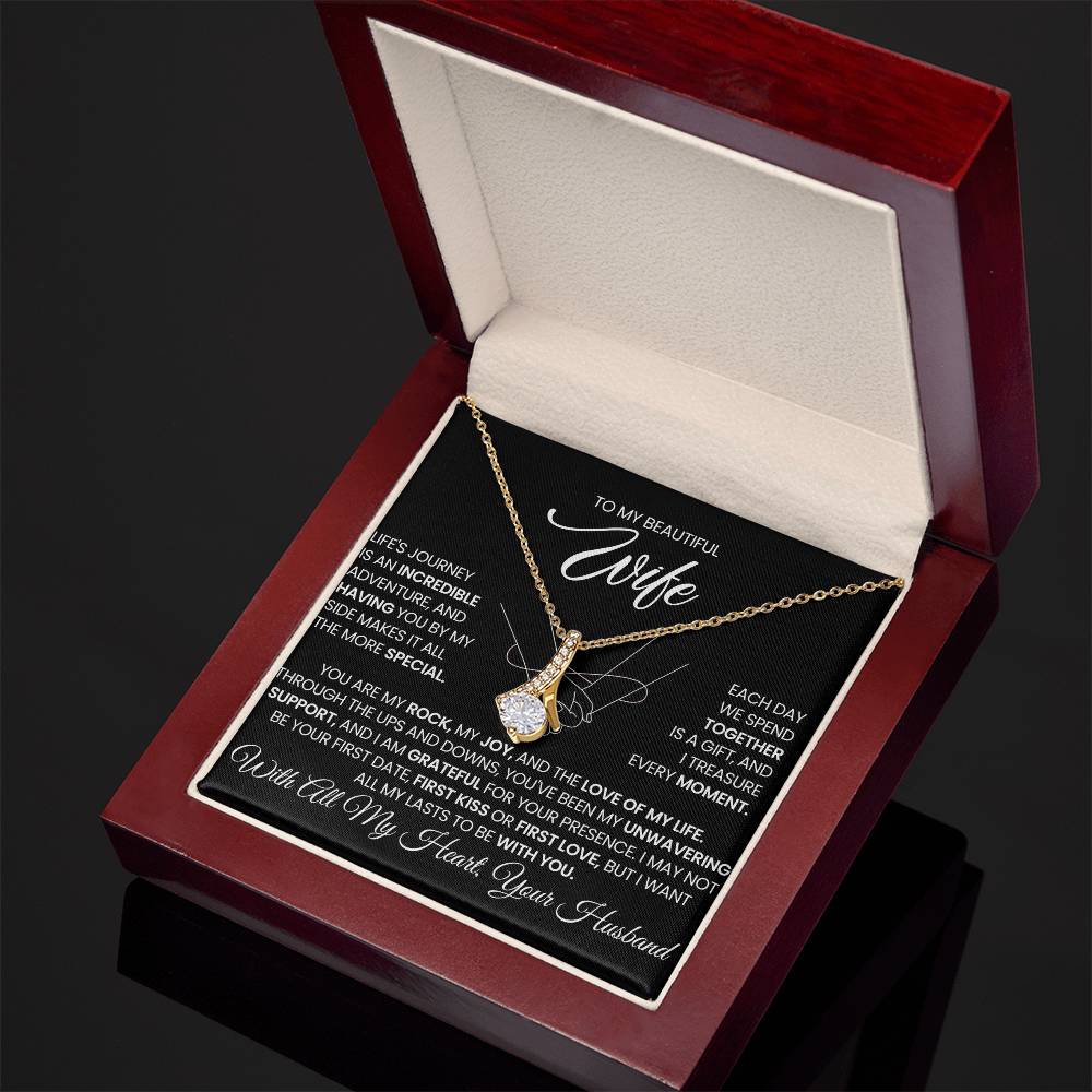 Angled open red presentation box displaying a gold-tone ribbon pendant necklace.
