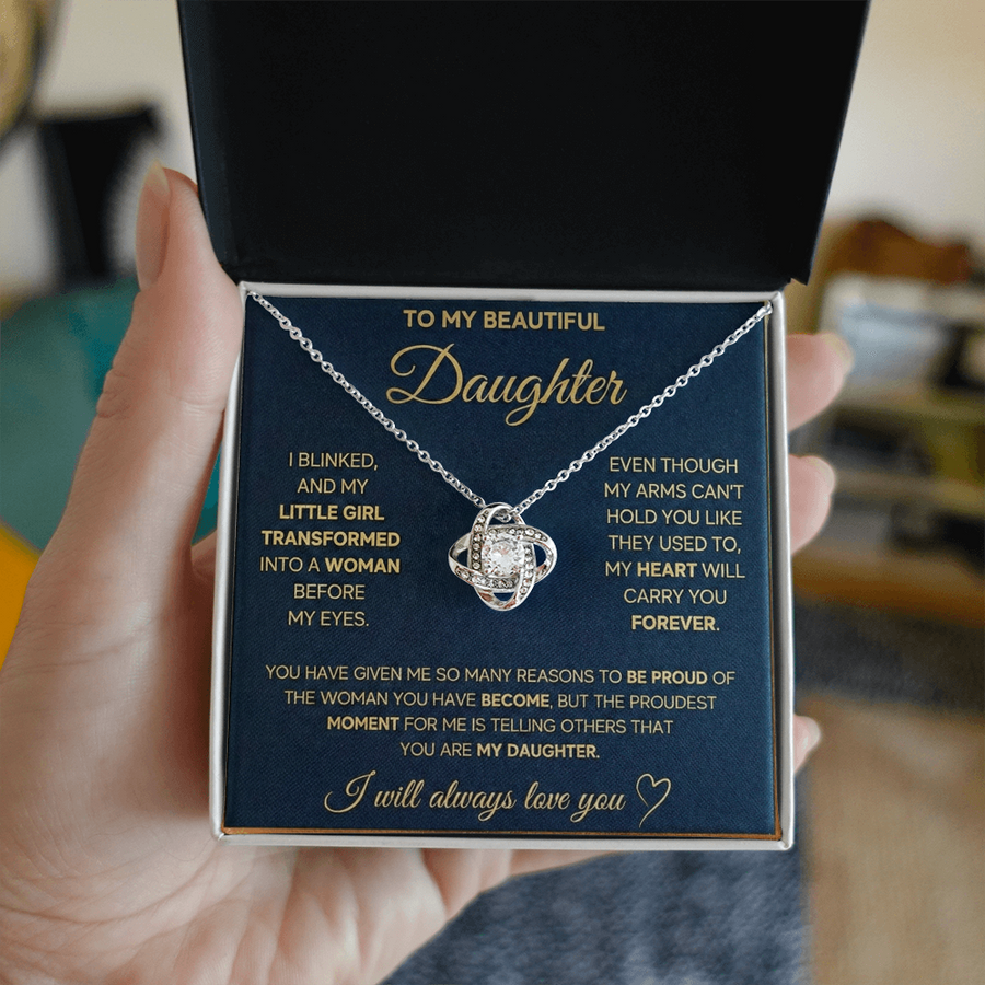 Hand holding an open gift box with a silver-toned Love Knot necklace
