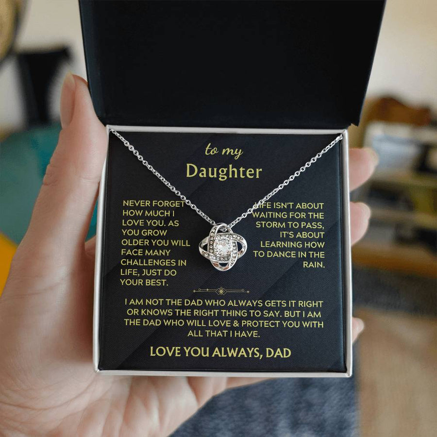 A hand holds an open jewellery box containing a silver-toned Love Knot necklace and daughter message card