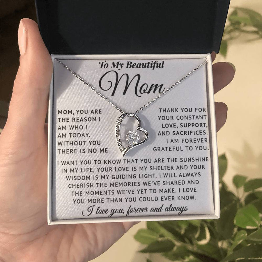 A hand holds a boxed heart necklace with a heartfelt message card for Mom