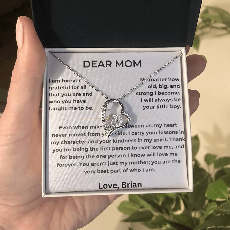 Silver heart necklace and Dear Mom message card held in a hand outdoors