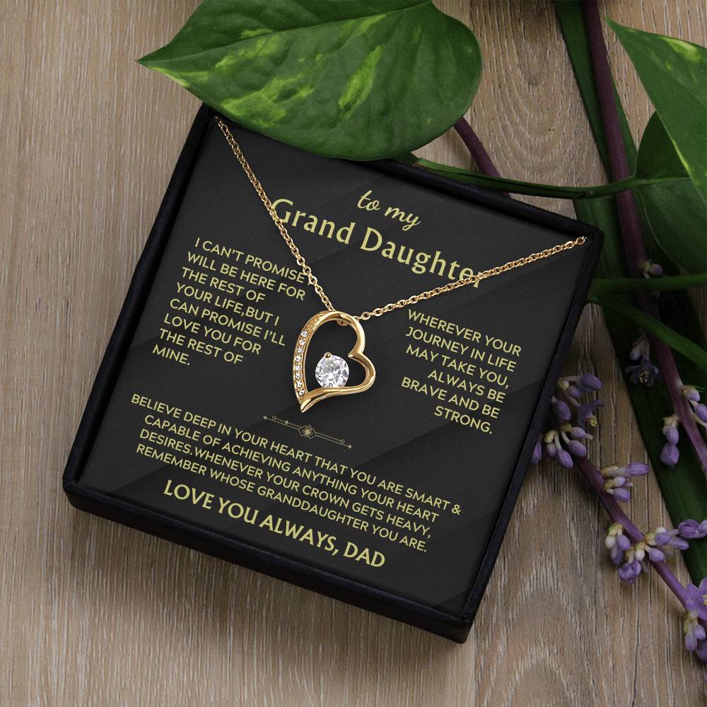 Gold heart necklace displayed in a black box on a wooden surface with a Grand Daughter message card
