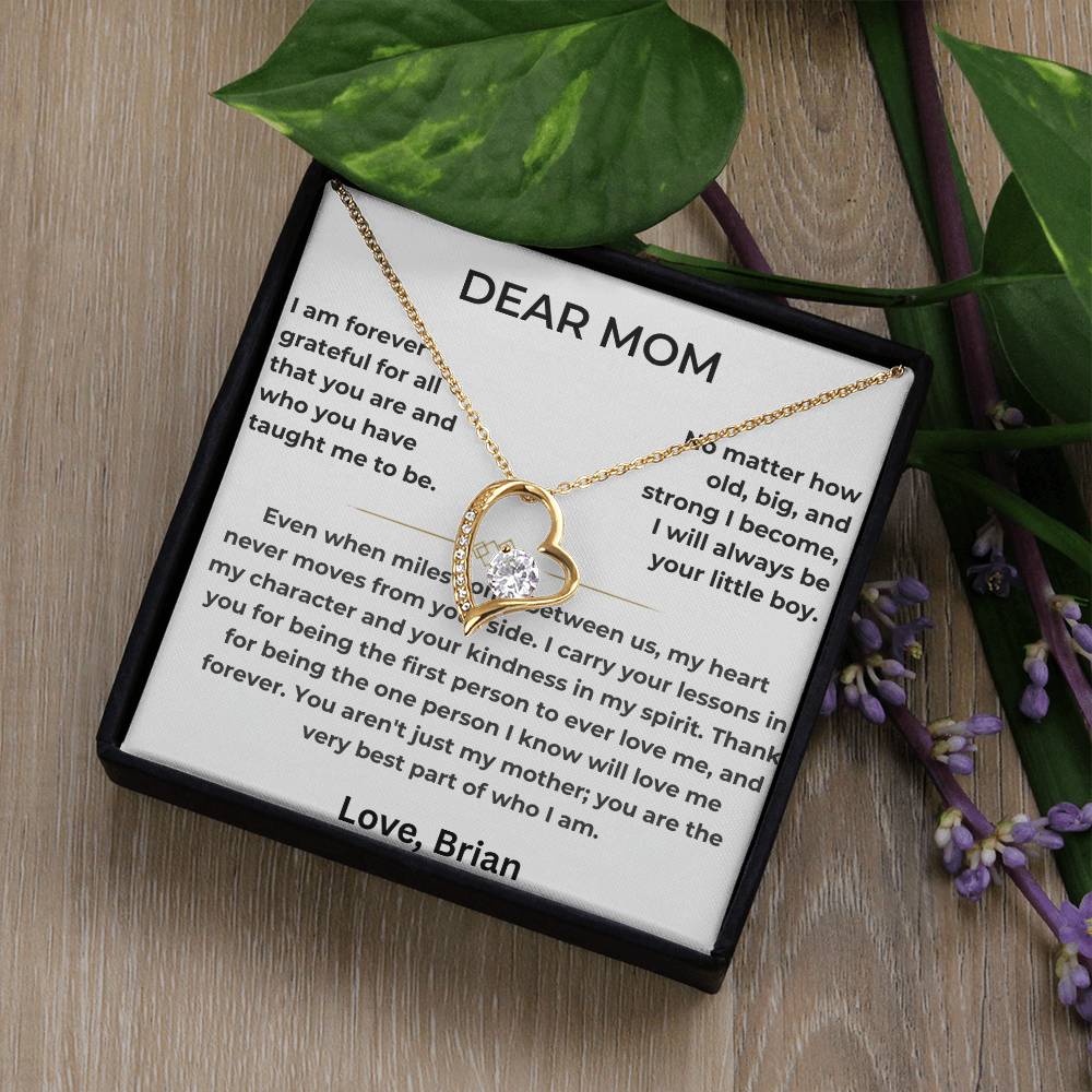Gold heart necklace displayed on a Dear Mom card beside green leaves