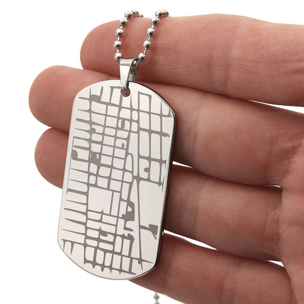 Silver map dog tag necklace held between fingers, showing the engraved front