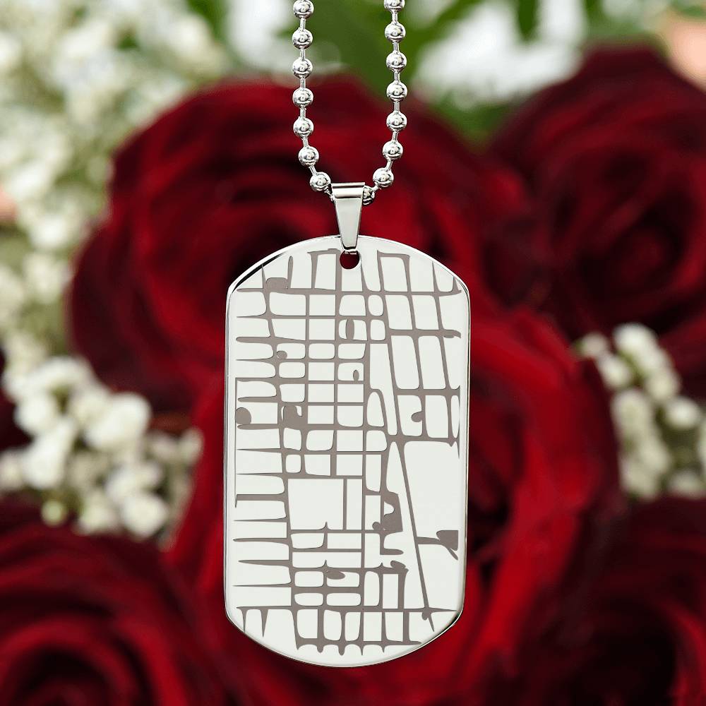 Silver map dog tag necklace photographed against red roses