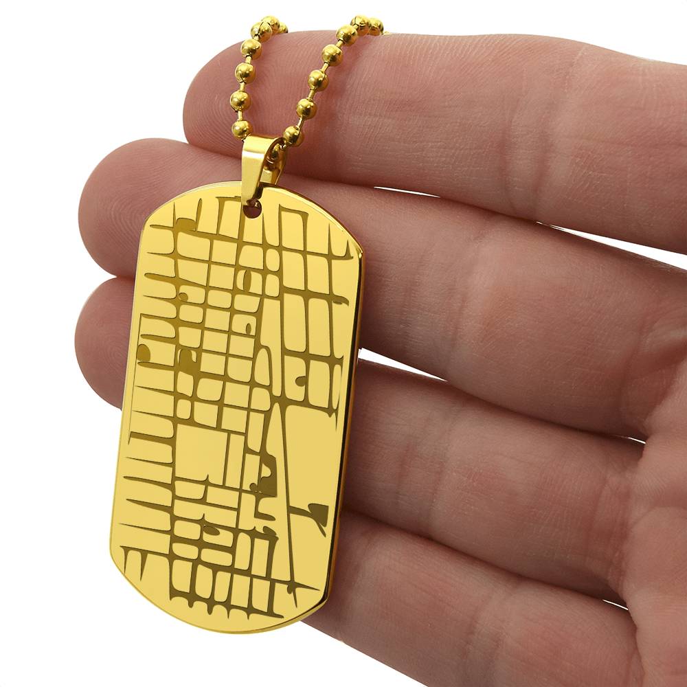 Gold map dog tag necklace held between fingers, showing the engraved front