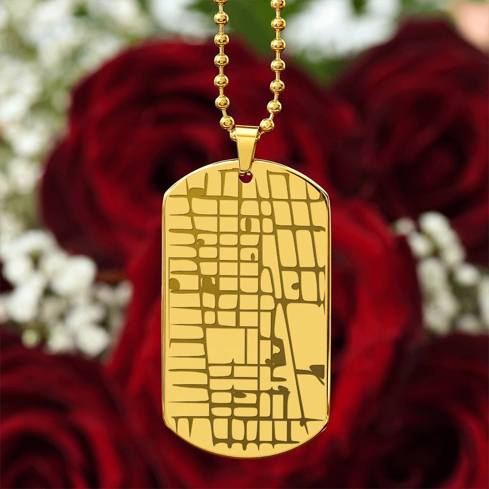 Gold map dog tag necklace photographed against red roses
