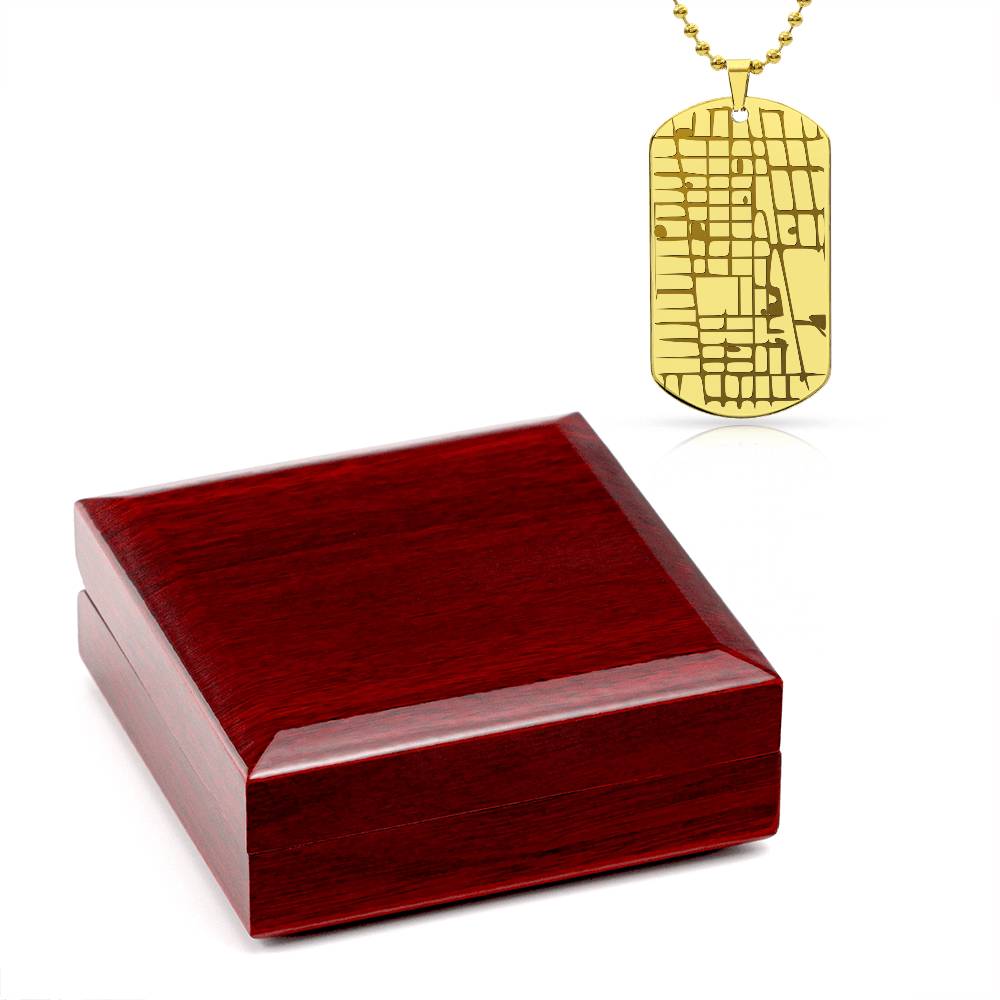 Gold map dog tag necklace displayed above a dark wooden presentation box